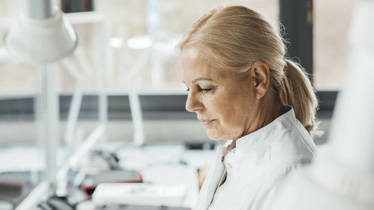 Scientist using laptop by robotic arms in laboratory 